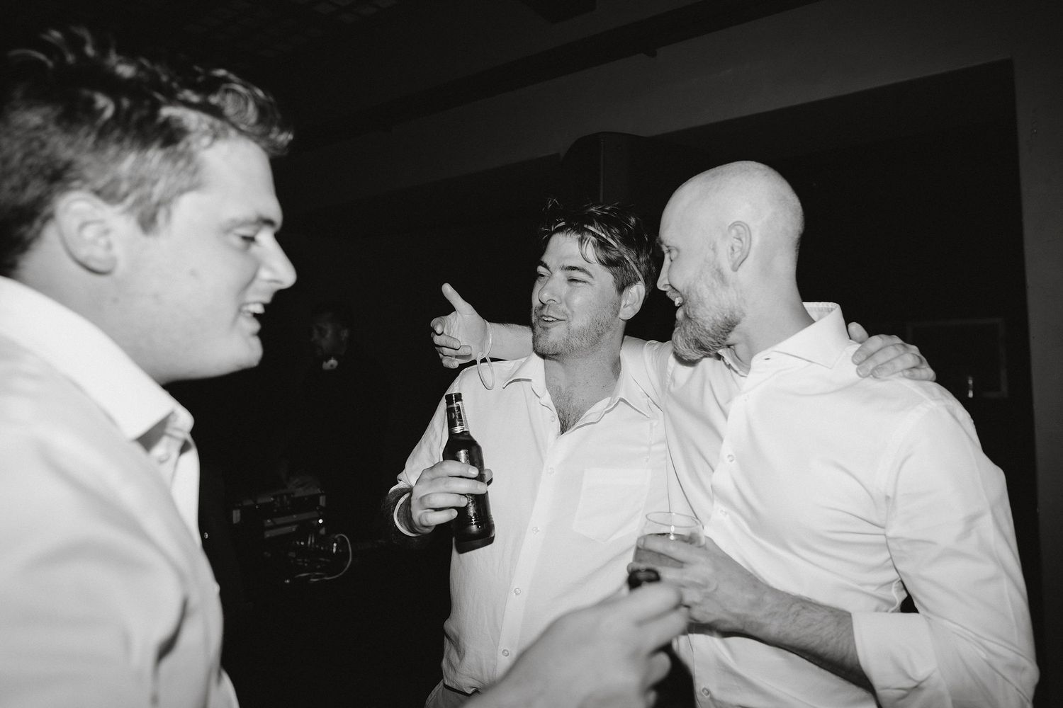 Three people in white shirts having drinks and engaging in conversation at a social gathering.
