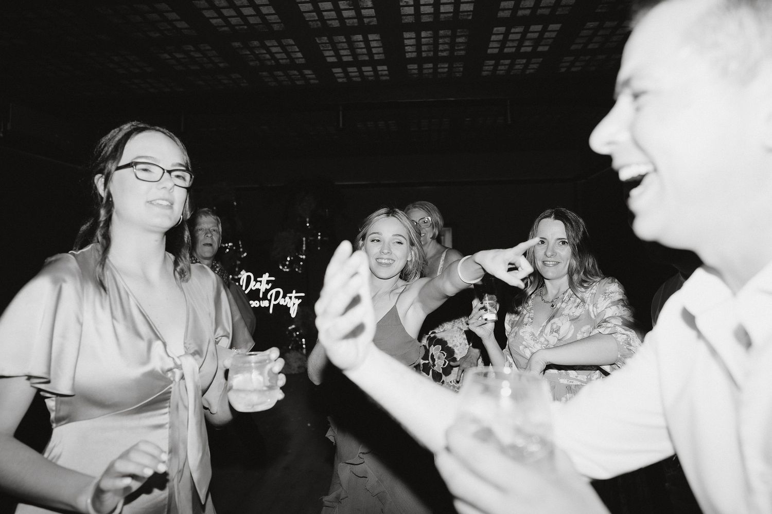 People smiling and laughing together on a dance floor at a celebration captured in black and white photography.
