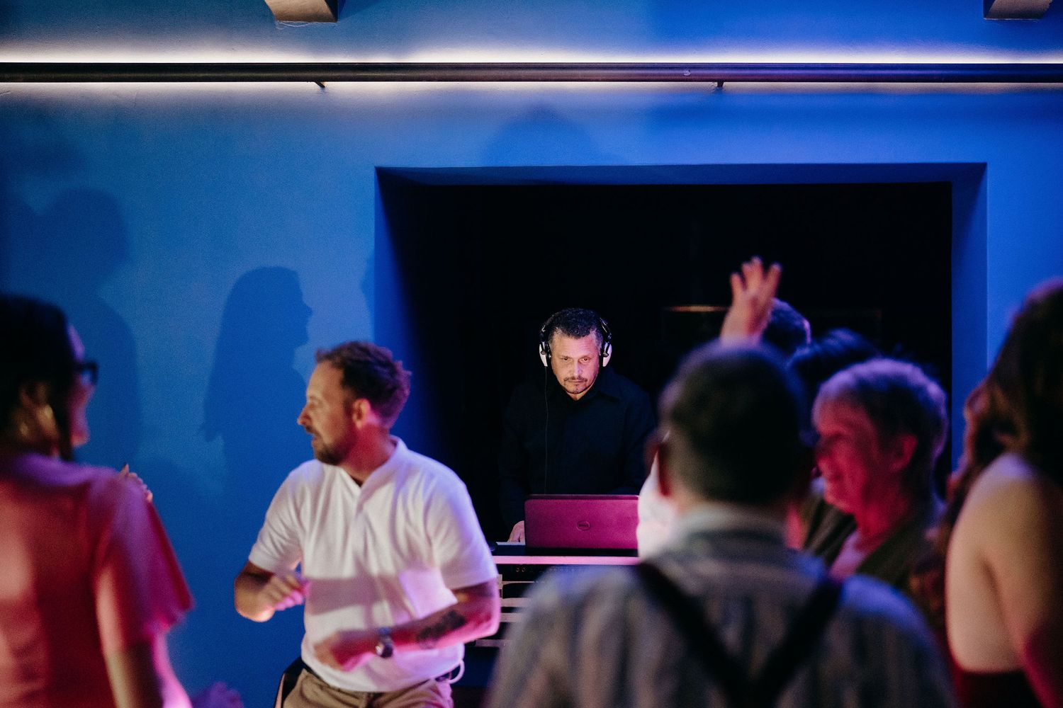 DJ performs at a nightclub with blue lighting while people gather on the dance floor.