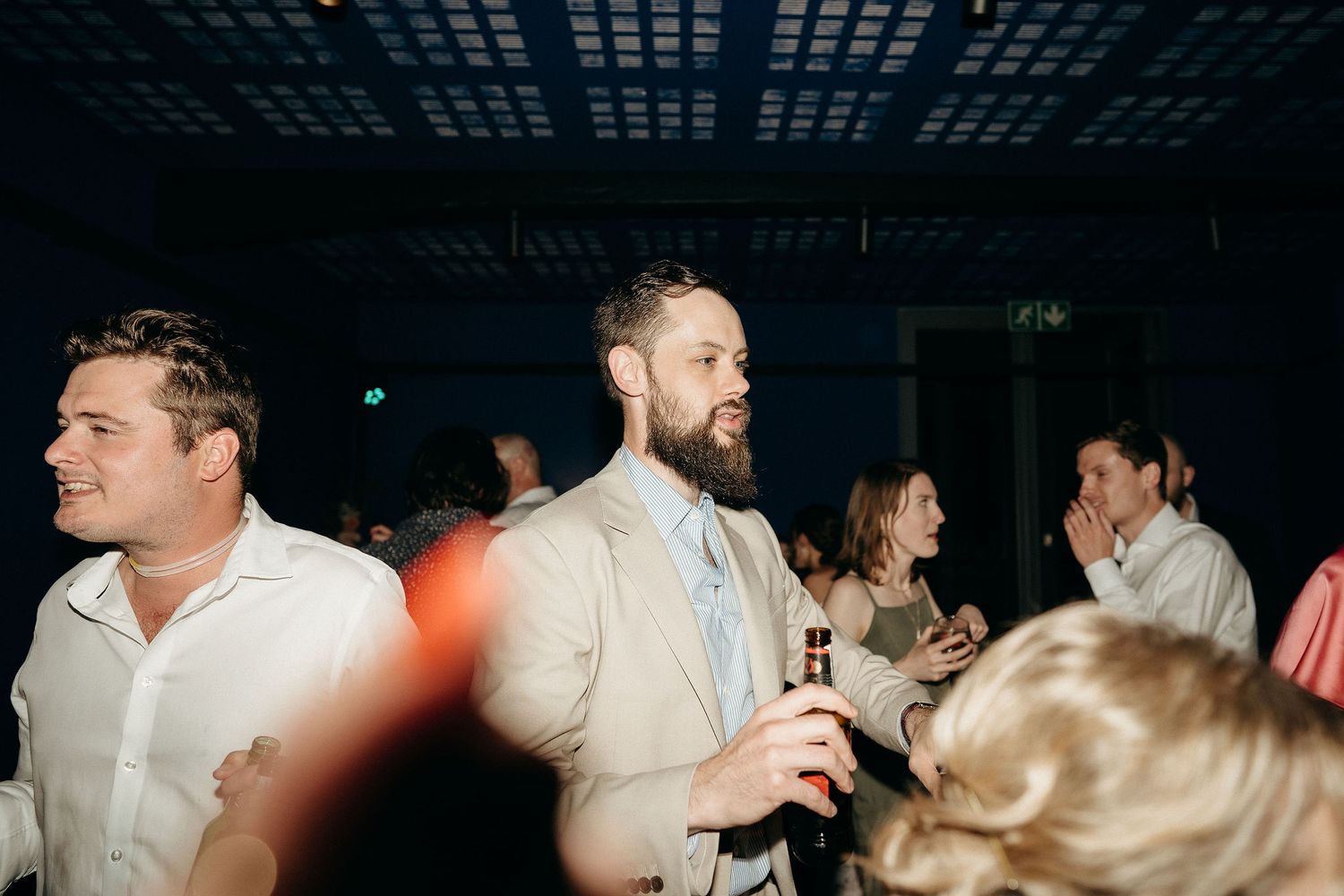 Party guests enjoying drinks and socializing at a nighttime indoor event with dark lighting and glowing accents.