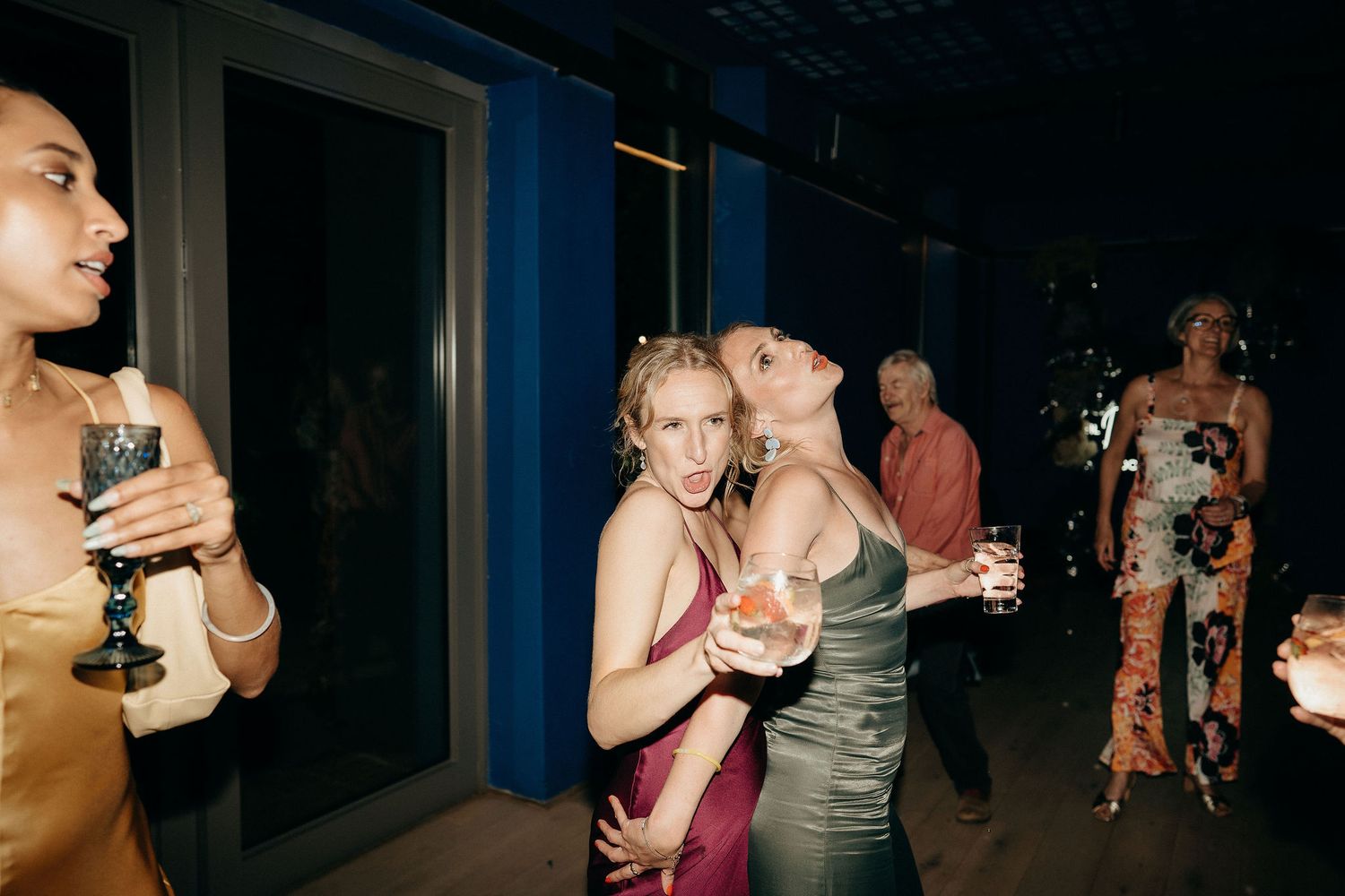 People enjoying drinks and socializing at a dimly lit party with blue walls in the background.