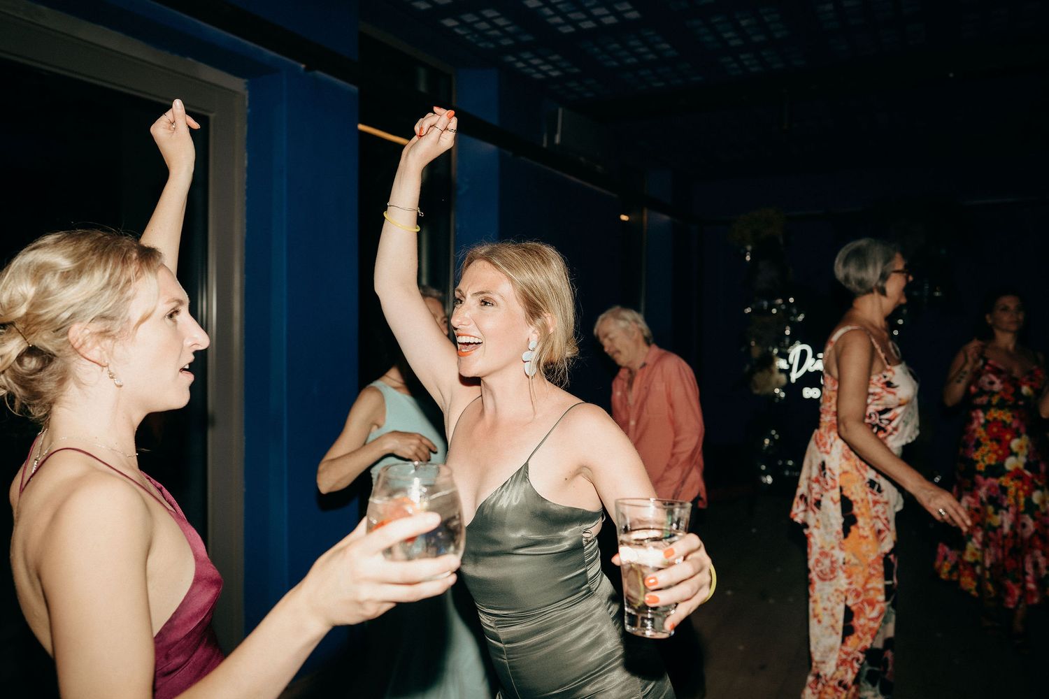 Two people hold drinks and dance together at a nighttime party or celebration event.