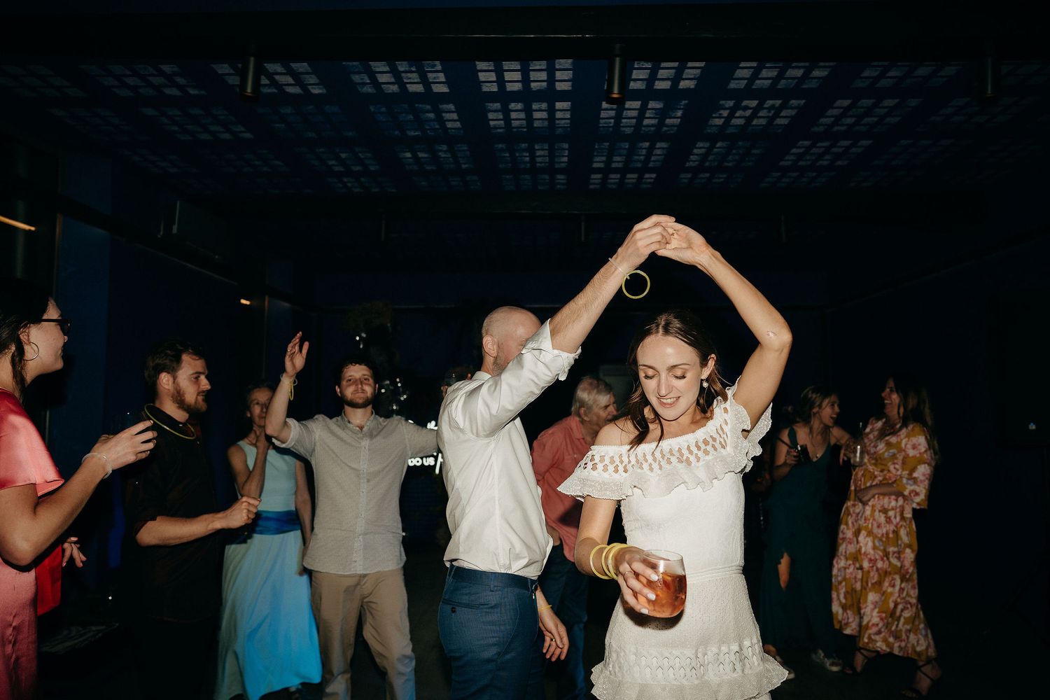 Wedding guests dance and celebrate on a dark dance floor during an evening reception celebration.
