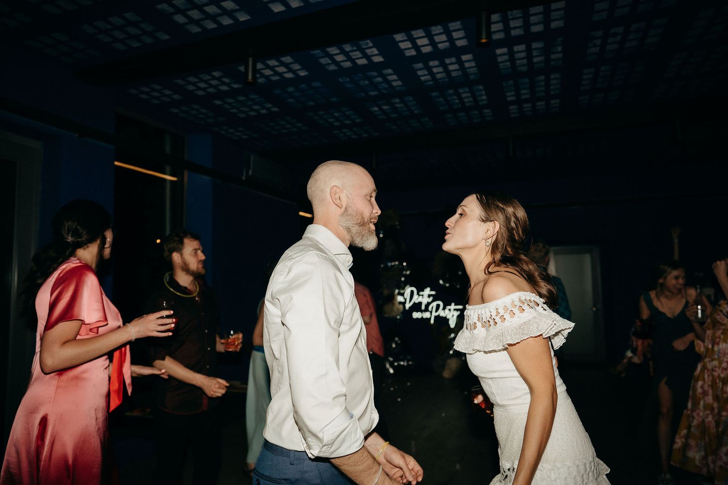 Couple shares a joyful moment together on the dance floor at a wedding reception with guests in the background.