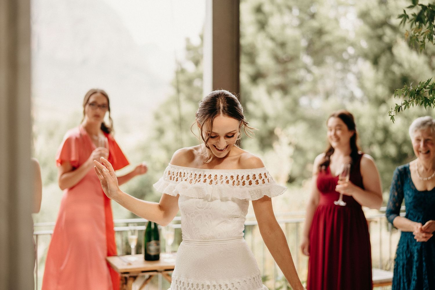 Joyful wedding preparation moment with attendees in colorful dresses gathered on an outdoor porch.