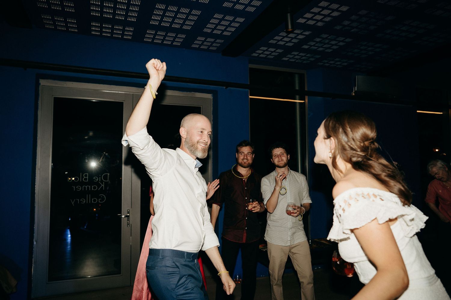 People dancing and celebrating on a dimly lit dance floor at a wedding reception.
