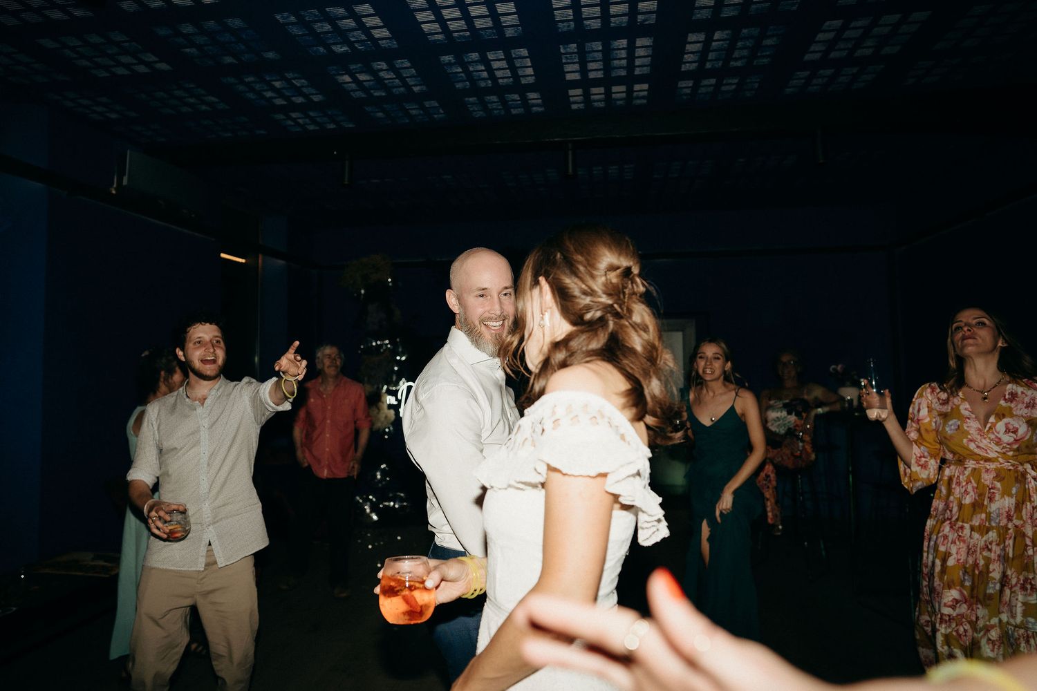 Couples dancing together at a lively indoor party with guests mingling in the background.