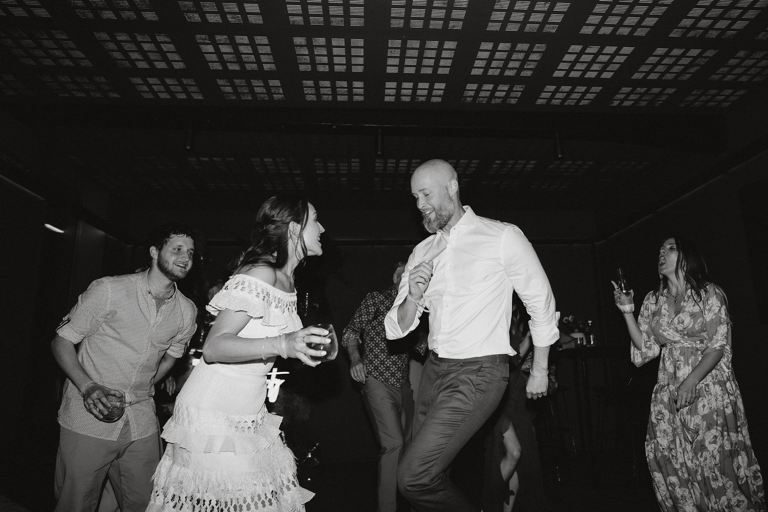 People dancing energetically at a dark indoor event space with filtered lighting overhead.