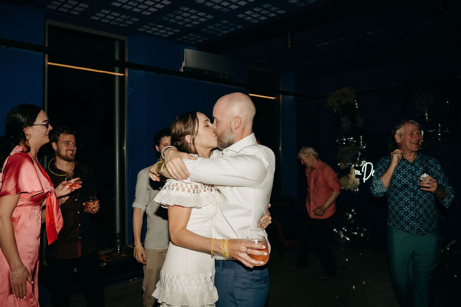 People dancing at a dimly lit wedding reception venue under decorative ceiling lights.