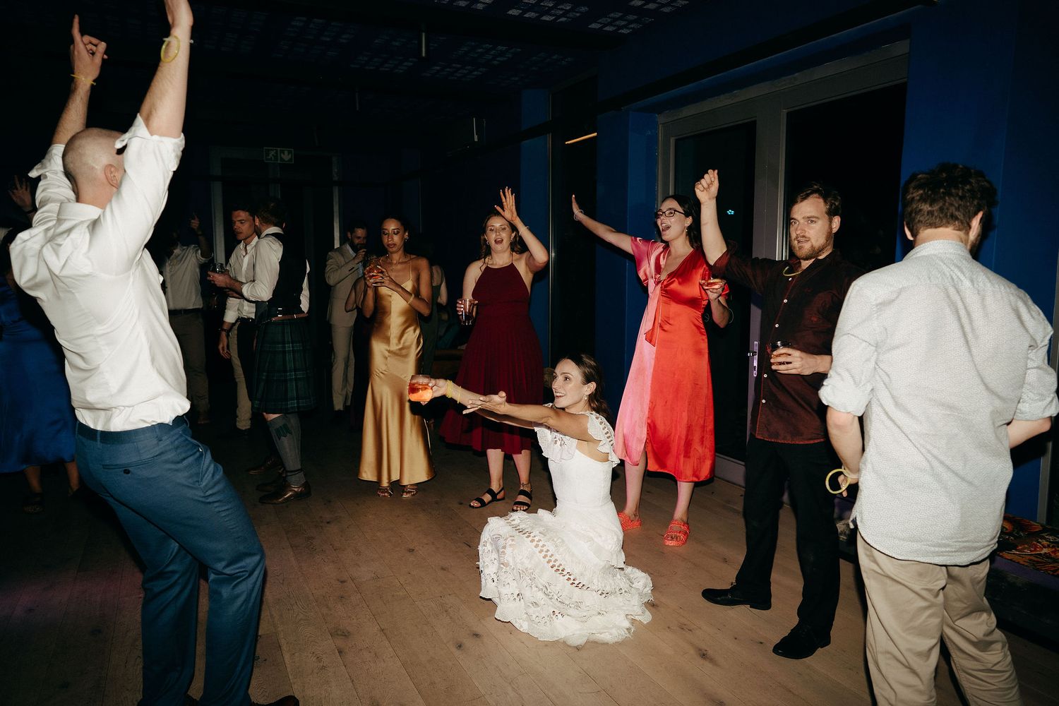 Wedding guests dance and celebrate on a dark wooden dance floor at a reception party.