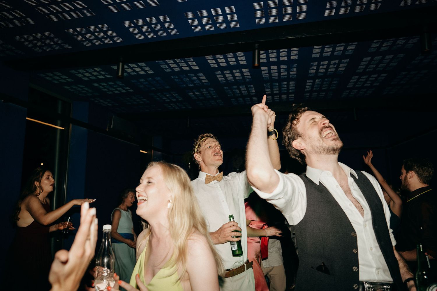 Party guests dancing and celebrating enthusiastically at a nighttime event with arms raised in the air.