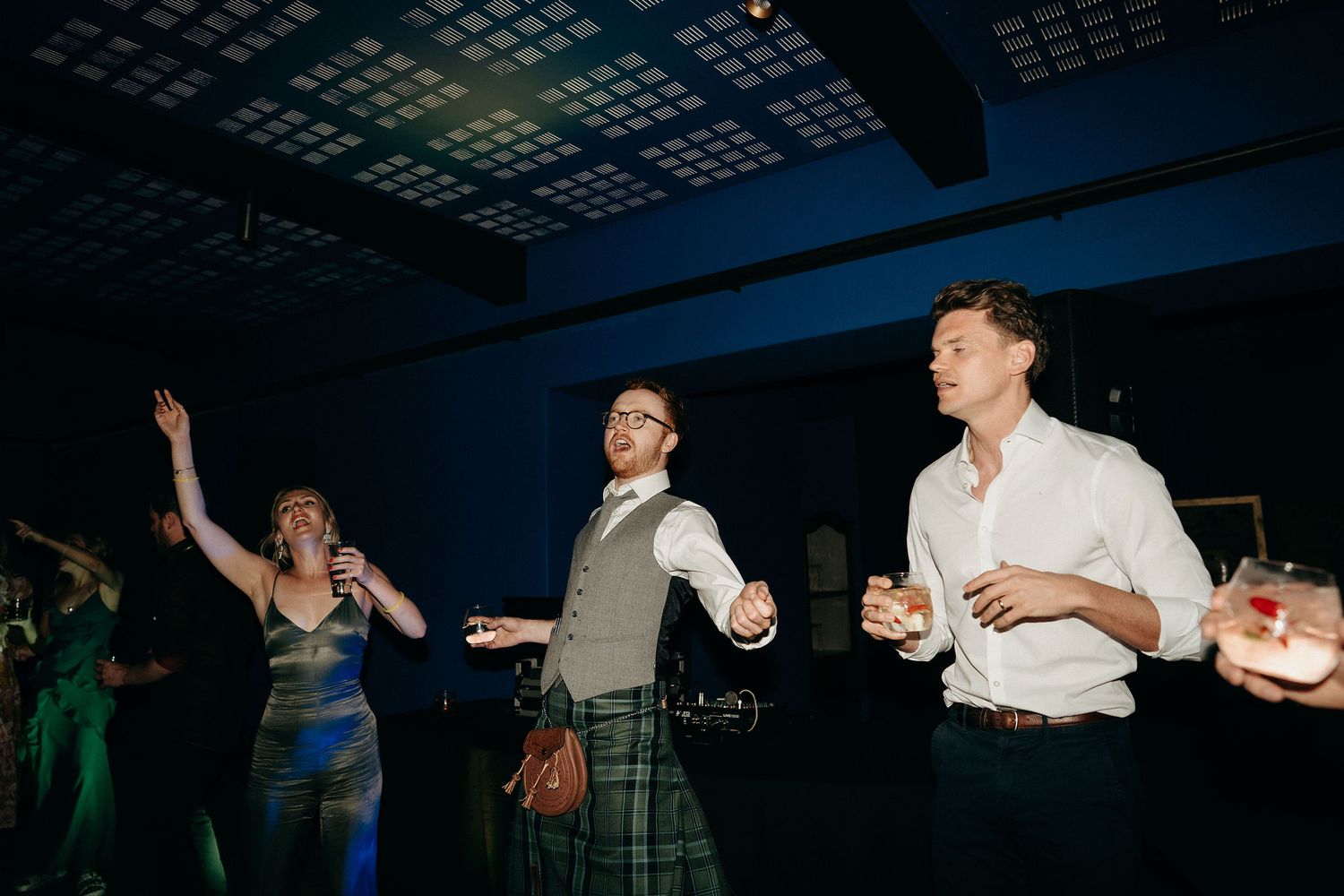 Wedding guests enjoy dancing and celebrating on the dance floor during an evening reception under blue lighting.