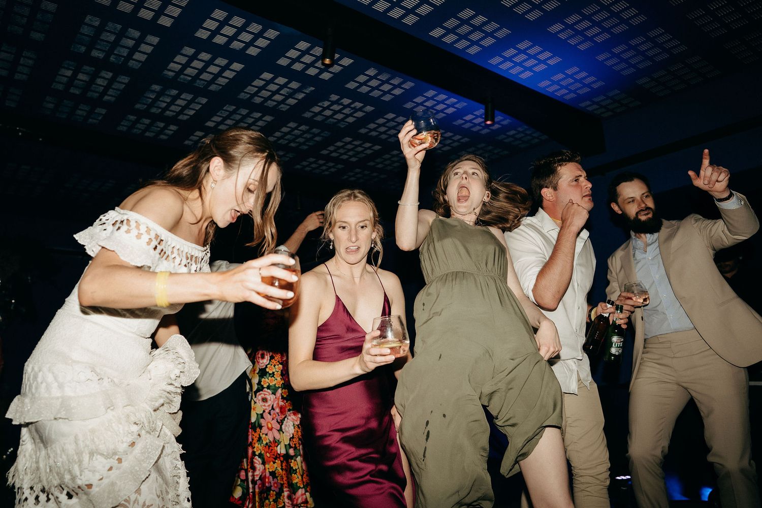 A group of people dancing energetically at a nightclub or party under blue lighting.