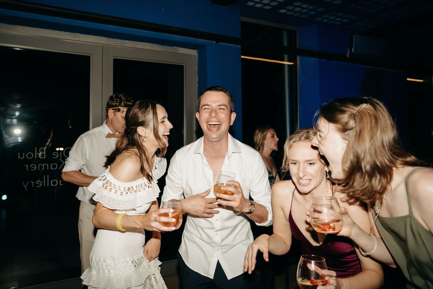 A group of stylishly dressed people laughing and enjoying drinks together at a nighttime social gathering.