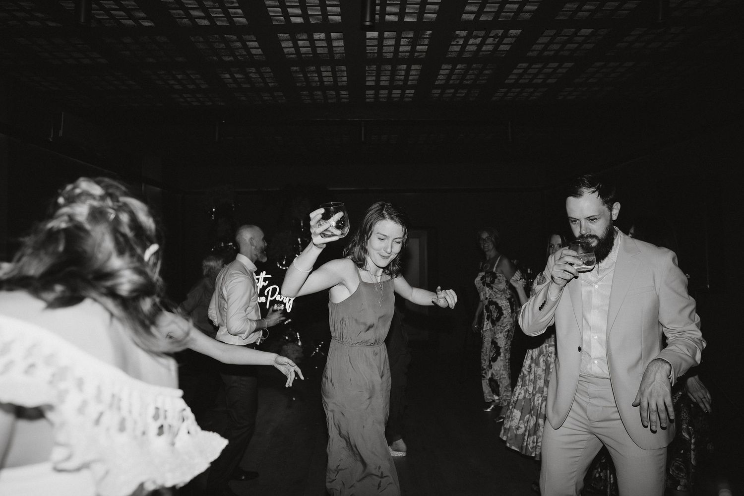 People dancing energetically at what appears to be a wedding reception in a dark venue, captured in black and white.