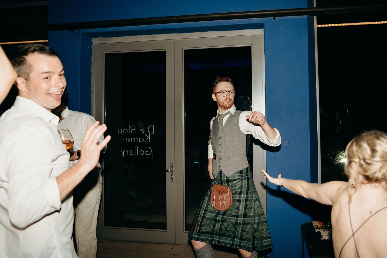 People dancing and celebrating at a party where someone is wearing a traditional Scottish kilt.