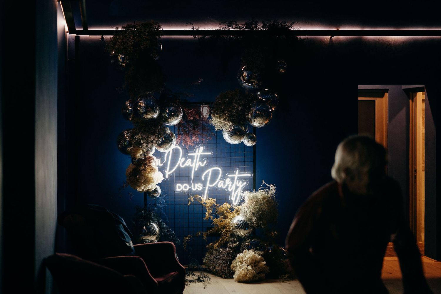 A neon sign reading "Just pop" glows on a dark wall decorated with floral arrangements and greenery.
