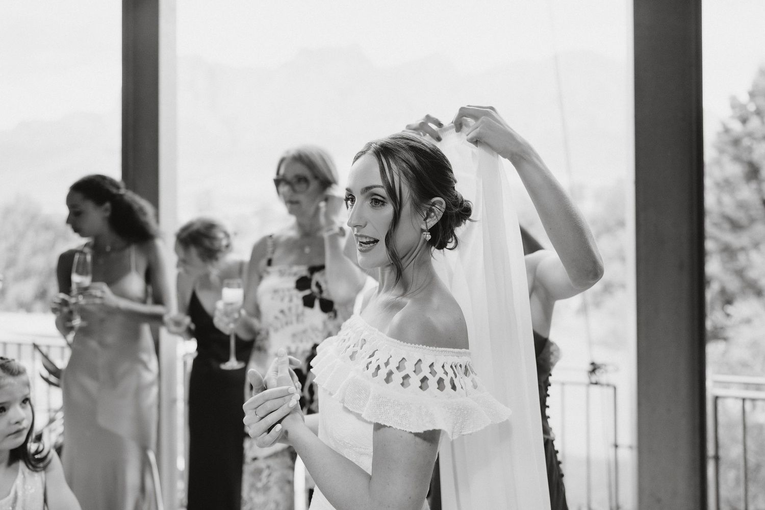 Black and white photo of wedding party lined up on a covered porch holding champagne glasses for a wedding toast.