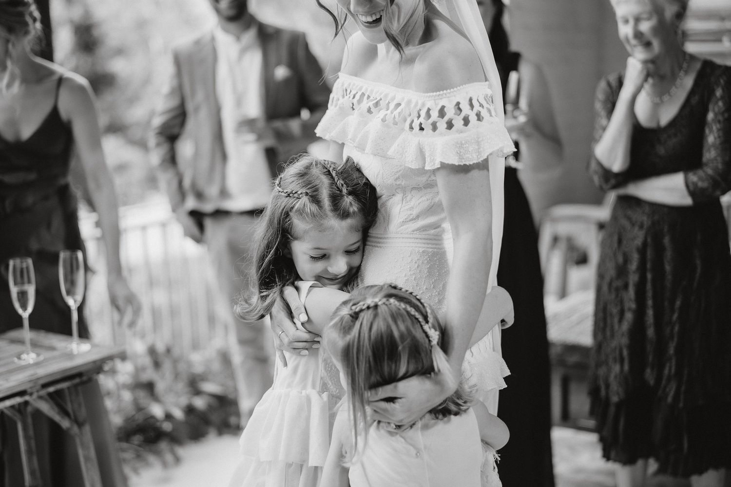 Two young children in formal wear share a tender moment at an elegant celebration with champagne flutes visible.