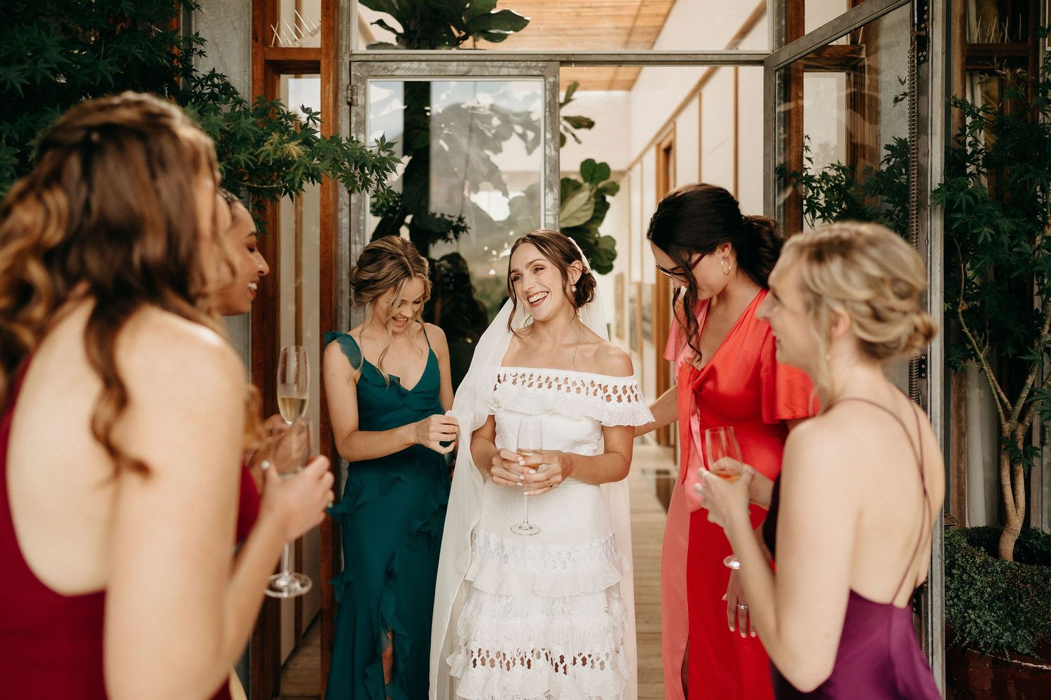 A group of friends in colorful dresses share a special moment in a bright indoor space decorated with greenery.
