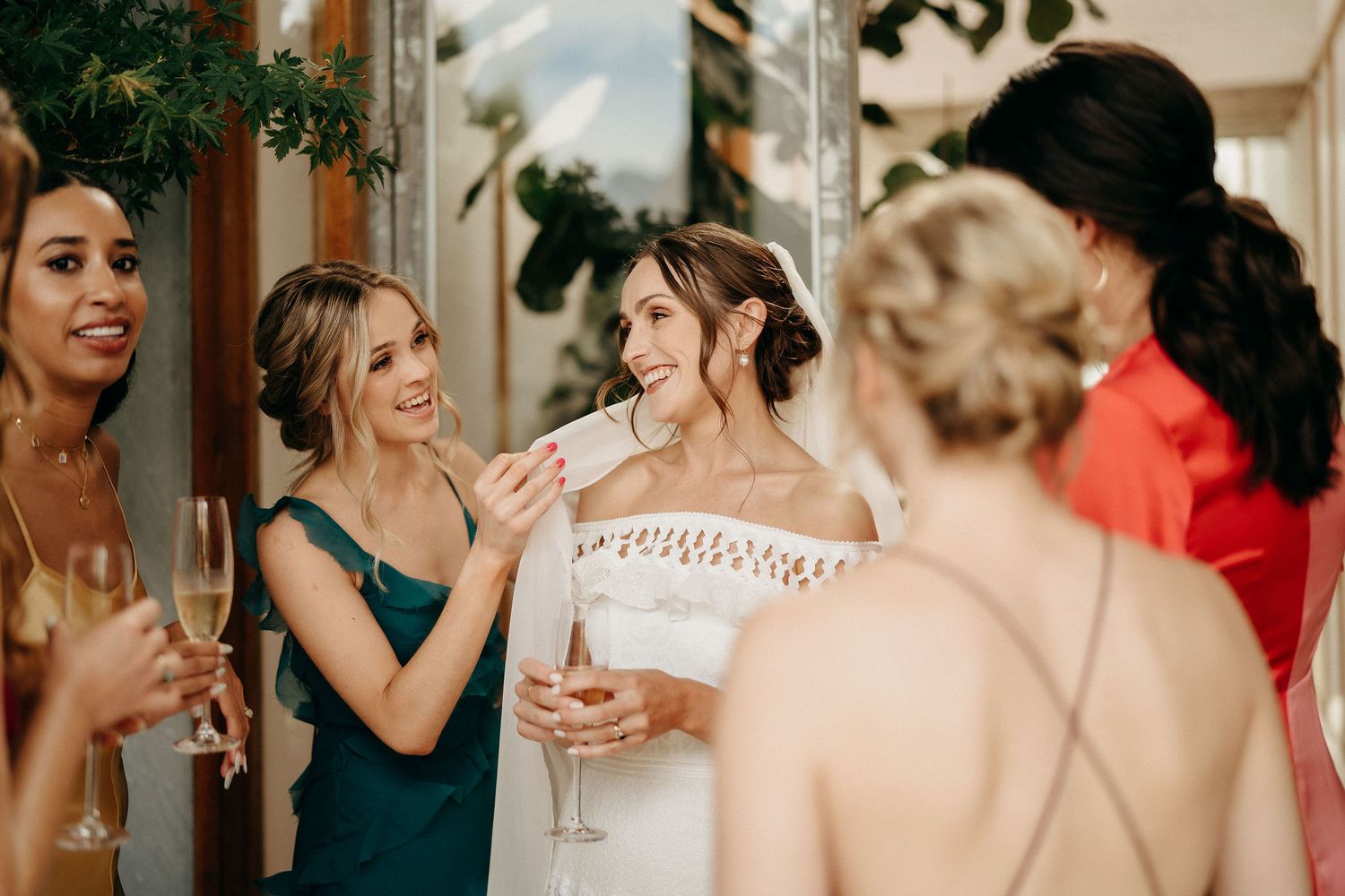 Wedding party guests share laughter and champagne during an elegant celebration at a venue with decorative columns.
