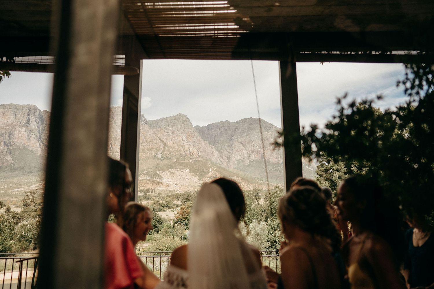 A group gathers beneath a covered porch overlooking scenic mountain views in the background.