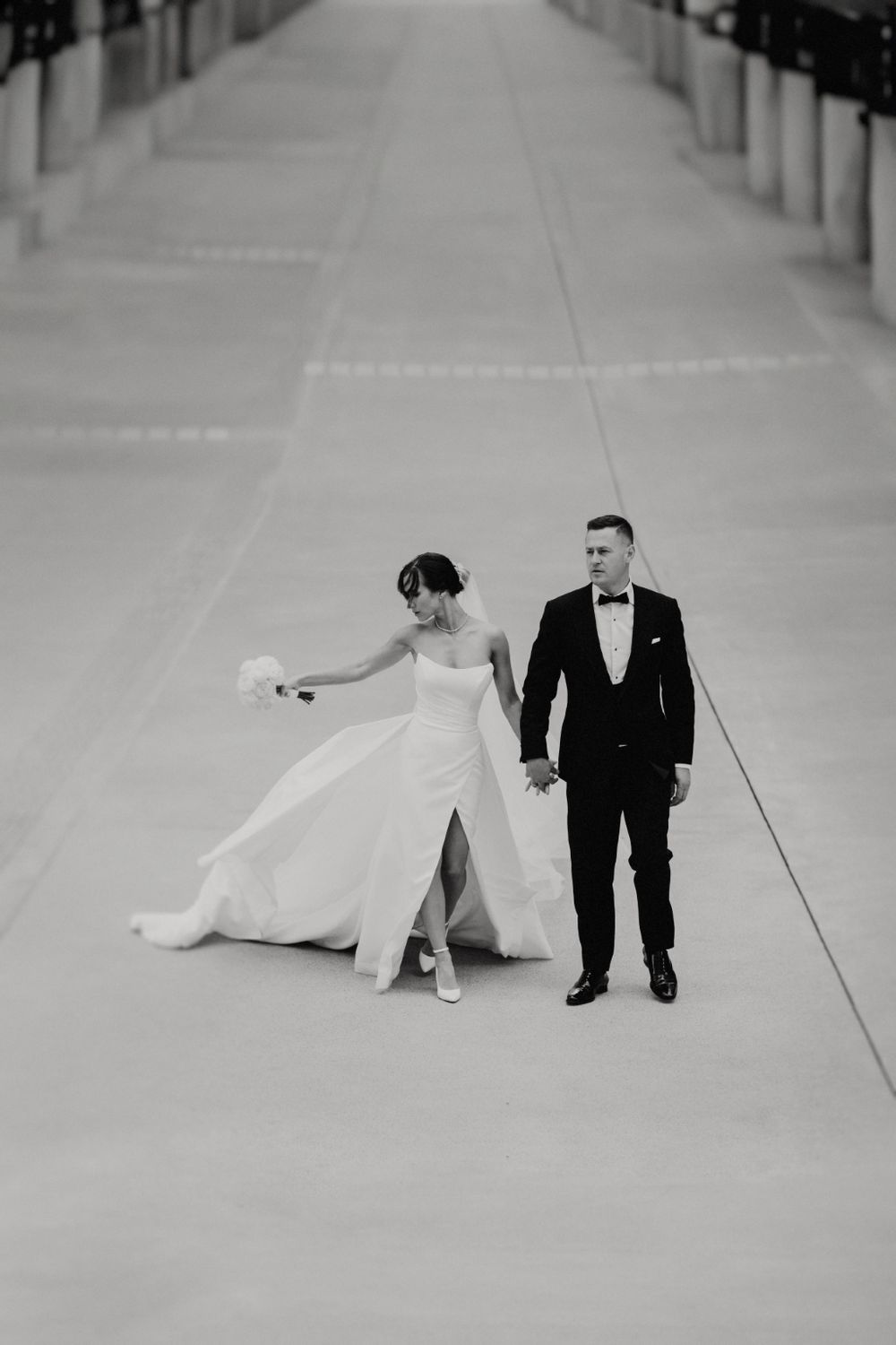 Black and white photo of couple walking down long corridor with flowing dress.
