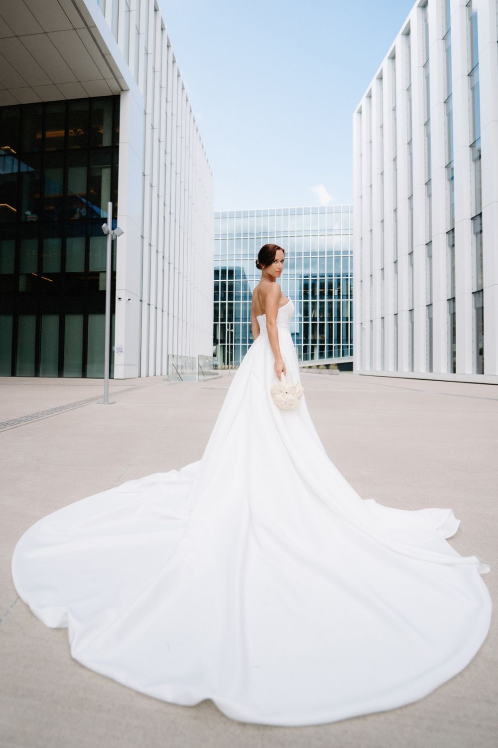 Stunning bridal gown with dramatic cathedral train photographed between modern white buildings.