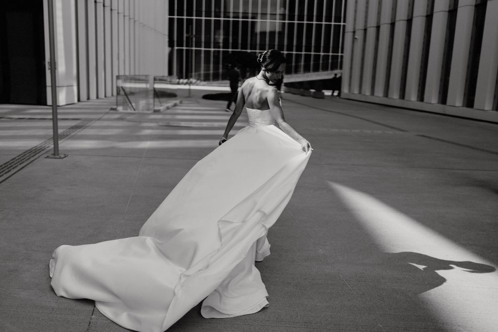 Bride's dress flows dramatically in black and white photograph against modern architecture.