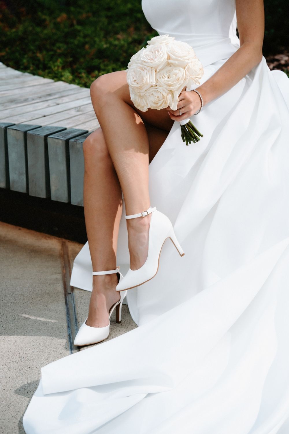 Close-up of bride's white heels and cream rose bouquet with flowing dress fabric.