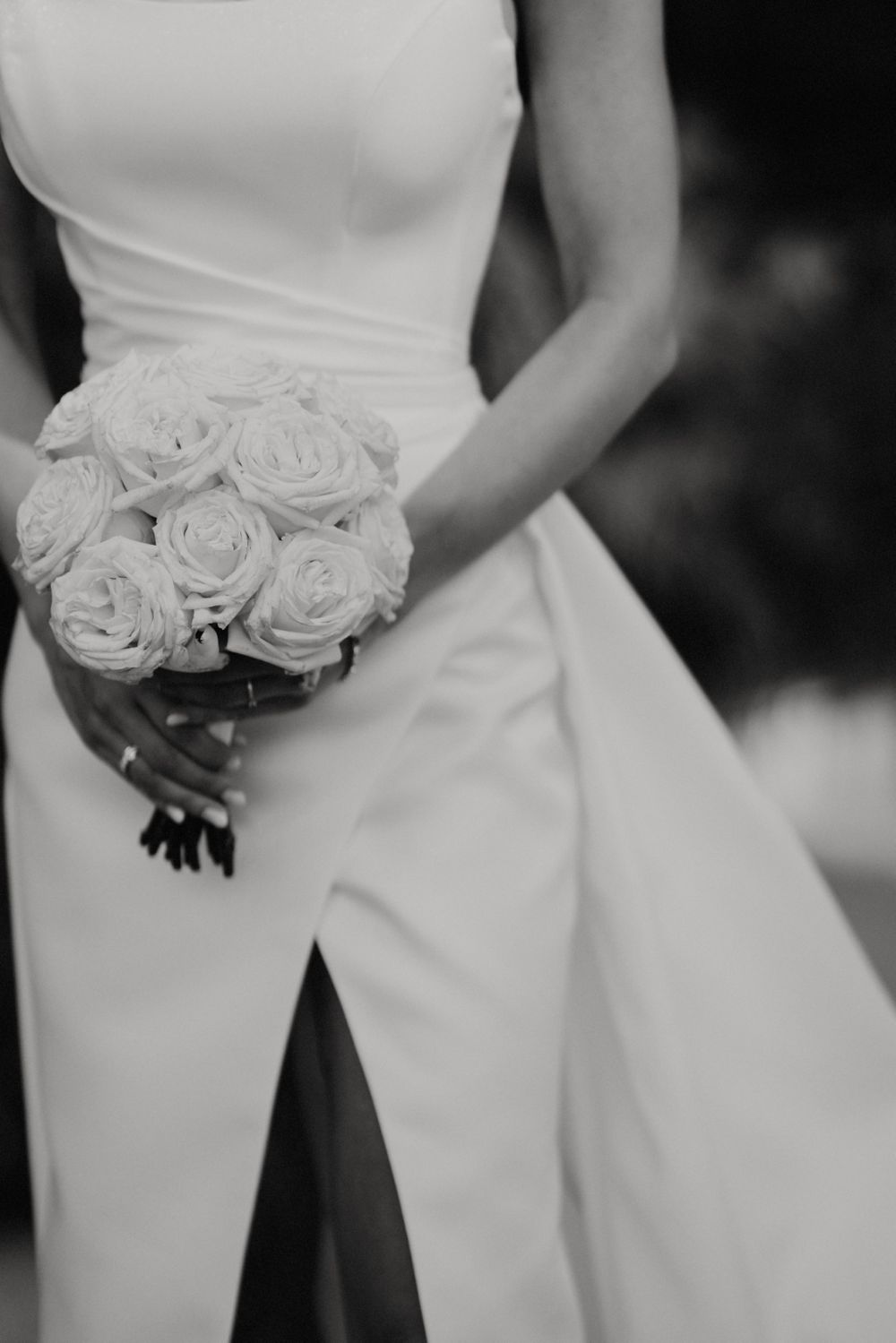 Elegant white rose bouquet held against structured wedding gown with architectural details.