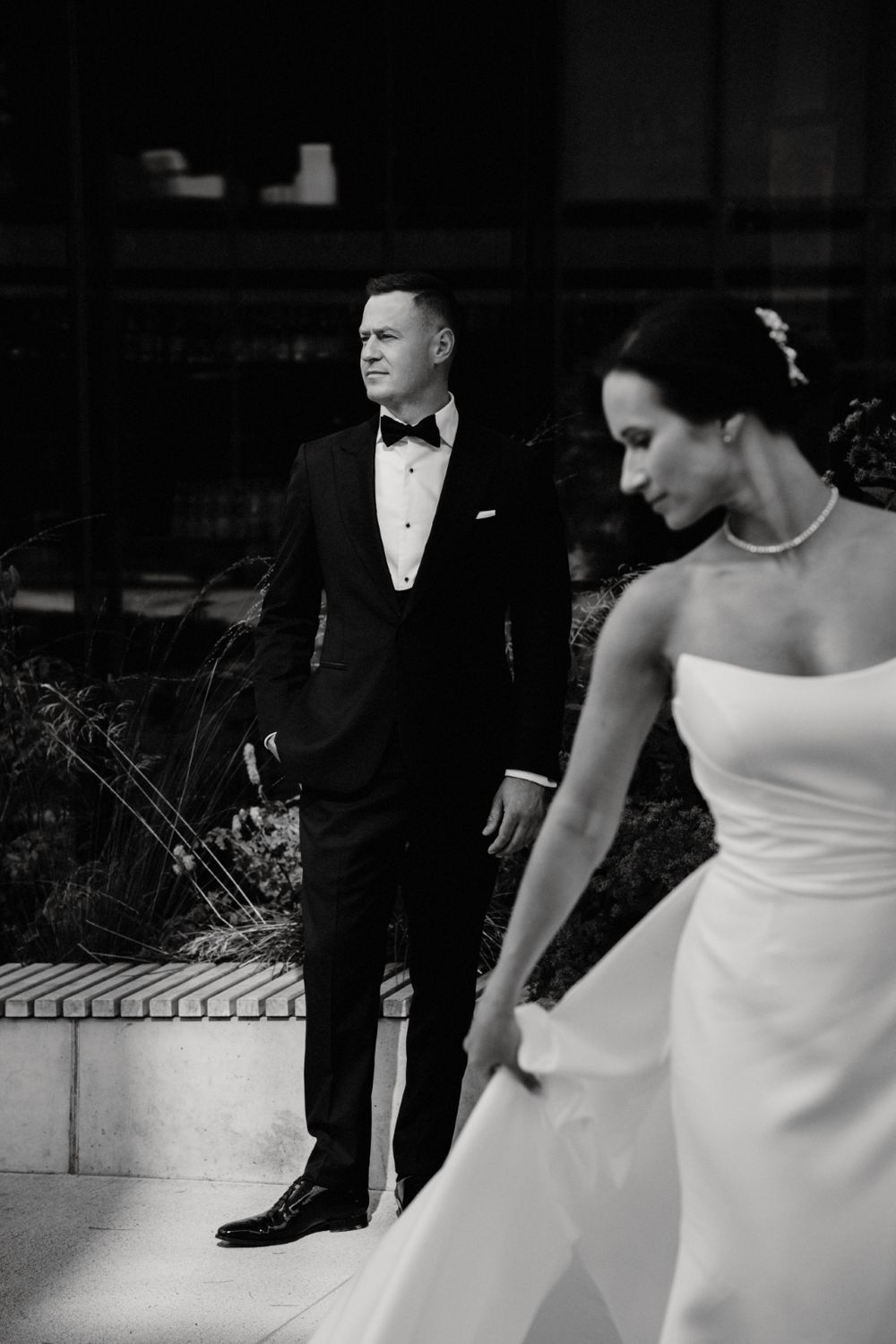 Black and white portrait of wedding couple in elegant attire against urban setting.
