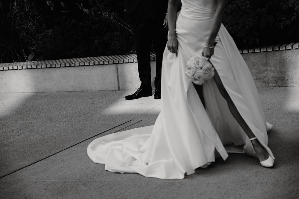 Black and white photo showing elegant wedding dress details and bouquet.