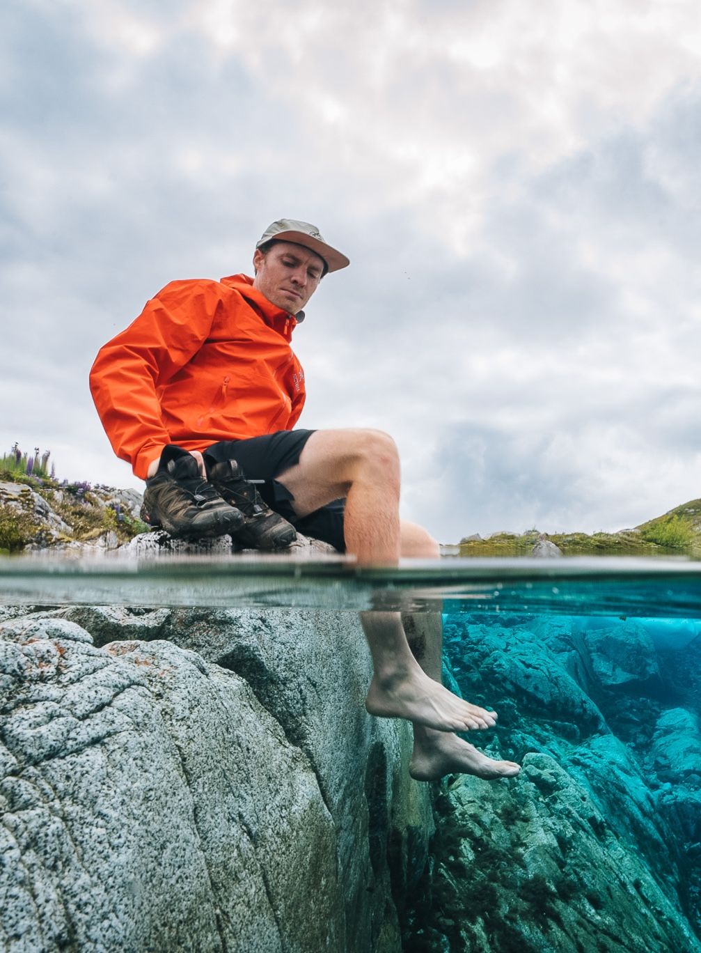 Split view photo of person in orange jacket sitting on rocky ledge with turquoise water visible underwater.