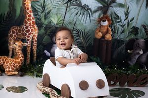 Baby smiles while sitting at a white table with jungle-themed decorations and stuffed giraffe toys.