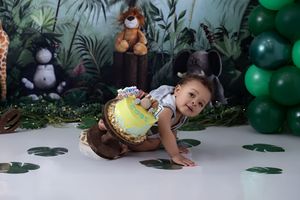 Jungle-themed birthday party setup with stuffed animals, green balloons and leaf decorations on white floor.