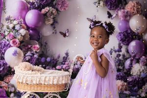 Lavender and purple balloon arch decorates a whimsical birthday party setup with floral accents and wicker baskets.