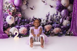 Festive purple and white holiday photo backdrop with balloons, garland, and Christmas trees creates an elegant winter scene.