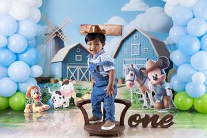 Farm themed first birthday party setup with blue balloon arch, barn backdrop, and rustic decorations.