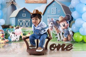 Farm-themed first birthday party setup with blue barn backdrop, rocking horse, Mickey Mouse decorations and balloon garland.