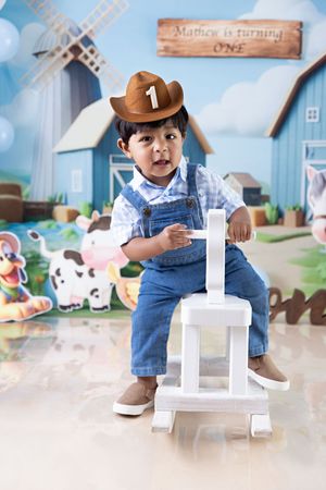 Small child in denim overalls and brown hat plays with white blocks in a whimsical farm-themed playroom setting.