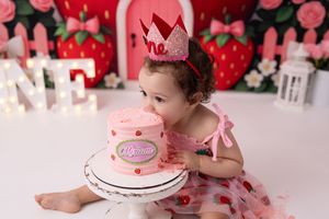 A pink and red themed birthday party setup with strawberry decorations and a white cake on the table.