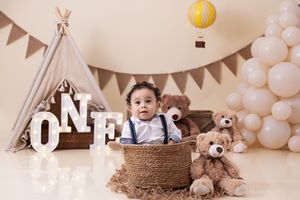 First birthday party setup with teepee, balloon decor, ONE letters and basket in neutral brown and white tones.