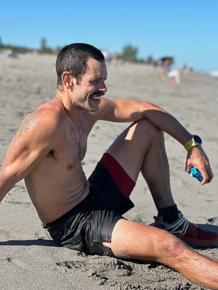 Runner rests on sandy beach after completing endurance event.