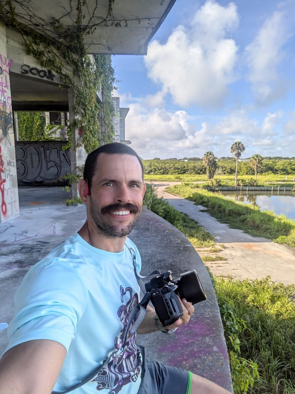 Person taking selfie with camera at abandoned structure overlooking water landscape.