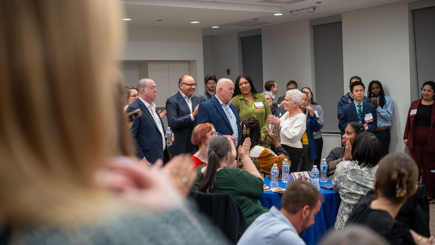 A group of people gathered in a meeting room applauding during a professional event.