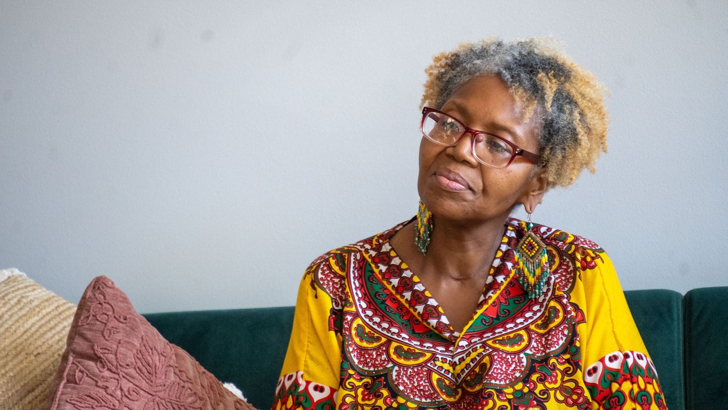 Someone relaxing on a green couch wearing a vibrant yellow African print dress with decorative neckline and glasses.