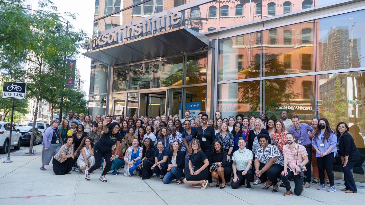 A large group of business professionals pose together outside a modern office building during the day.