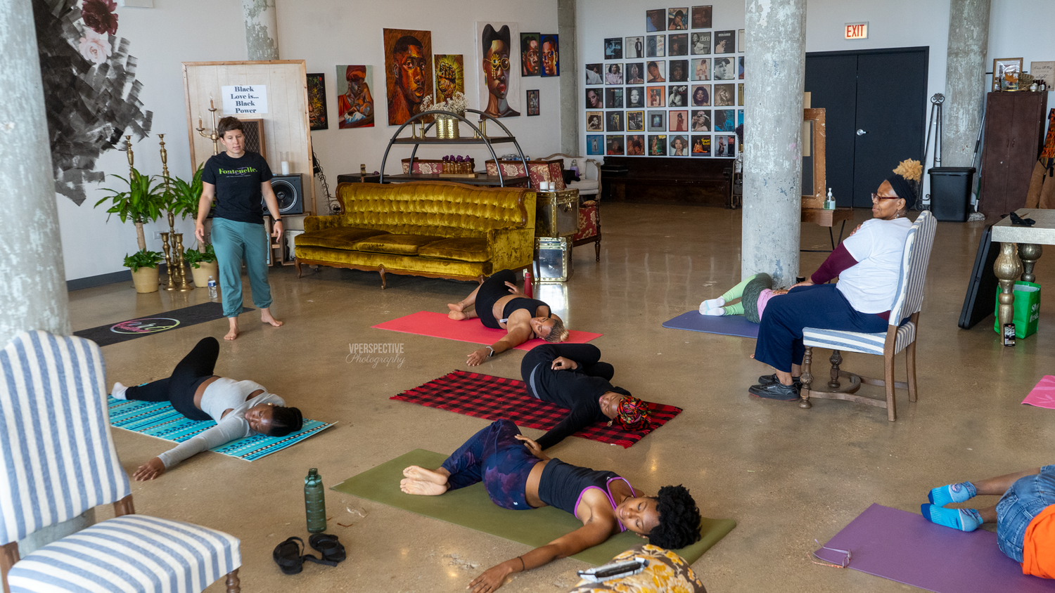 A group relaxes during a restorative yoga class in a studio space with a yellow couch and artwork on the walls.