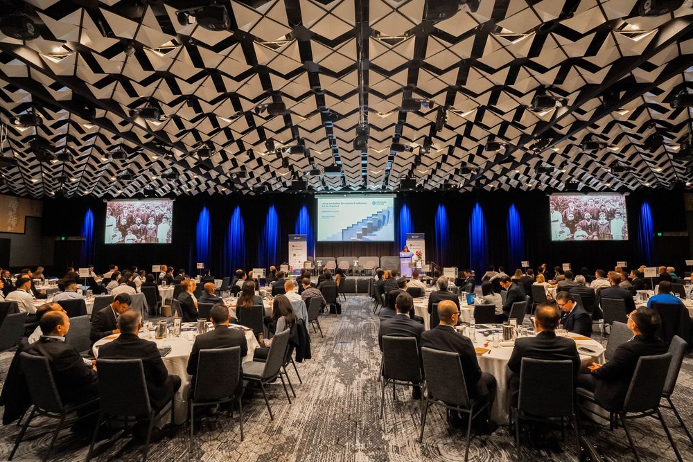 Large conference hall with geometric ceiling pattern and rows of tables set up for a formal event.